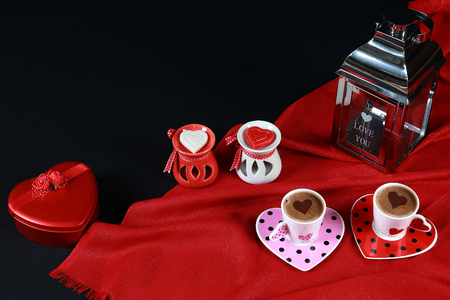 Valentine's day concept. Coffee in heart shaped cup with candle and red gift box on black background.の写真素材