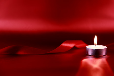 Valentine's day concept. Candle in candlestick with red ribbon on red shiny backgroundの写真素材