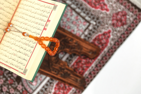 Islamic Holy Book Quran on wood carving rahle with rosary beads and prayer rug on isolated white background. Kuran the holy book of Muslims. Ramadan concept.の写真素材