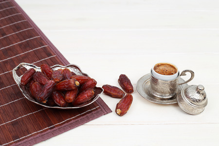 Islamic festival of Ramadan concept. With a delicious tropical dates on a silver plate and Turkish coffee on a white wooden table background. Traditional Middle East culture. Ramadan Kareem.の写真素材
