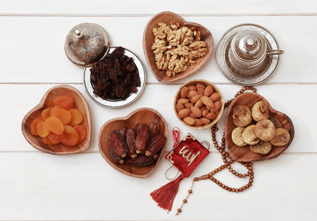 Ramadan iftar party concept. Islamic holy book Quran and rosary beads with delicious dates, dried figs, dried apricots, walnuts, almonds, raisins on bamboo plates on a white wooden table background.の写真素材