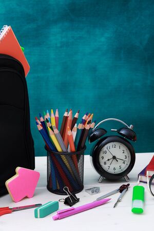 Back to school concept. School bag, pencils, crayons, scissor, notebooks, alarm clock, eraser, markers, watermark ruler, pencil sharpener, magnifying glass in a combine with a cyan backgroundの写真素材