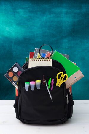 Back to school concept. School bag, pencils, crayons, scissor, notebooks, alarm clock, eraser, markers, watermark ruler, pencil sharpener, magnifying glass in a combine with a cyan backgroundの写真素材