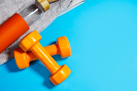 Orange dumbbells, towel and bottle of water on blue backgroundの写真素材