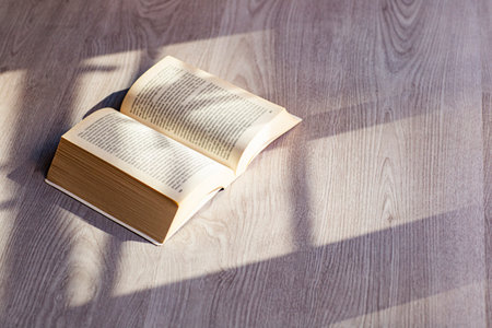Open book on a wooden table with shadows from the blinds.の写真素材