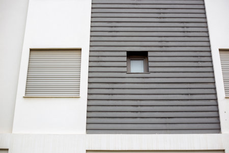 Window of a building with white wall and gray wooden shutters.