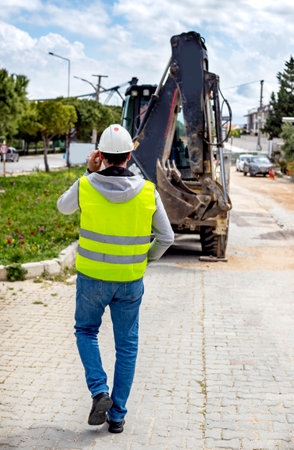 construction worker talking on mobile phone in front of excavator machine