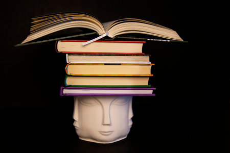 Books on the head of ceramic Buddha on a black background, audio books or education conceptの写真素材