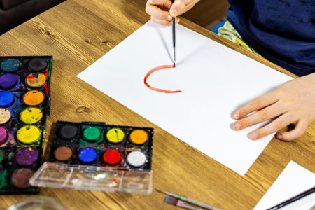 A child draws a picture with watercolors on a wooden tableの写真素材
