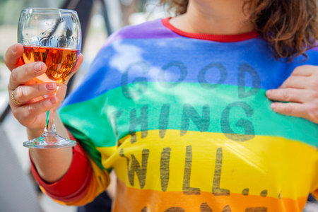 Woman in rainbow colored clothes holding a glass of pink wine in her hands outdoors. selective focus. LGBT supportの写真素材