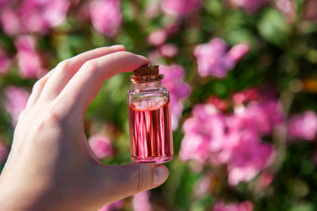 A bottle of essential oil with a pink flower in the background.の写真素材