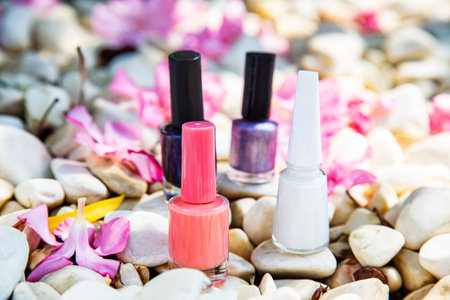 Colorful nail polishes on white stones background with pink fowers, manicure and beauty conceptの写真素材