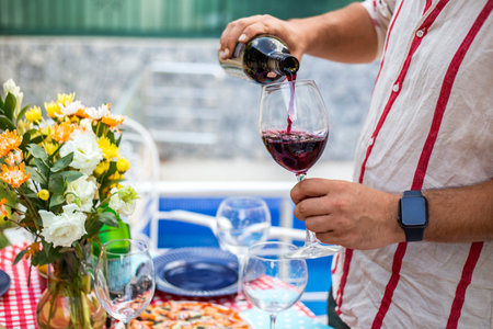 close-up of man hands pouring red wine into glass on his party garden backyard at sunset with set table in Spanish styleの写真素材