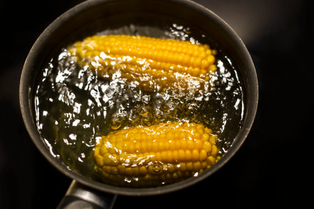Boiling corn in a boiling water in the pan. on black background close-up, selective focus.の写真素材