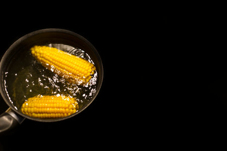 corn is boiling in a pan with hot water on a black background with space for text top viewの写真素材