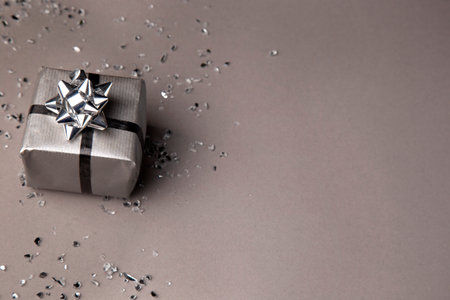 Silver gift box with silver ribbon and confetti on gray background.