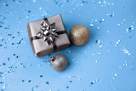 Silver gift box with silver bow and Christmas balls on blue background.
