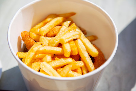 French fries in a white cardboard bucket on the table. close up
