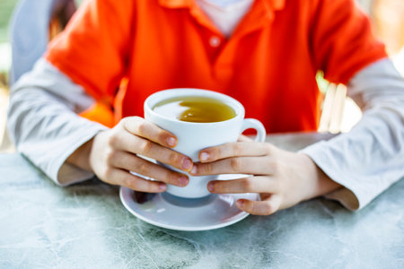 Close-up of person's hands holding cup of tea in cafeの写真素材