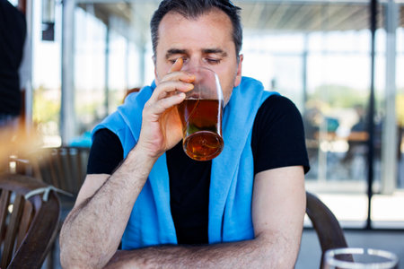 portrait of handsome man drinking beer in a pub. He is wearing a blue and black shirt.