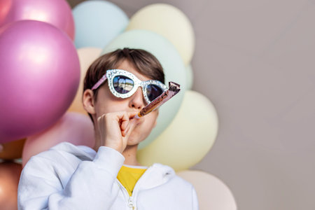 Cute boy in a white shirt and party glasses with party horn and colorful balloons on a backgroundの写真素材