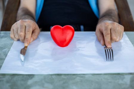 Close-up of male hands holding knife and fork with red heartの写真素材