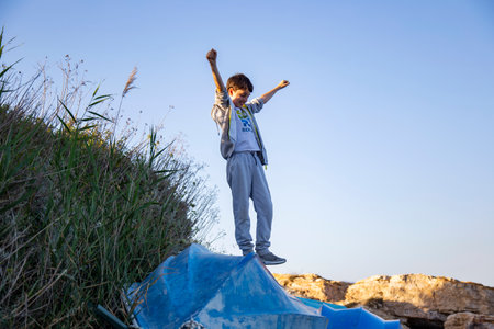 Little boy jumping in the air on top of a hill with his arms outstretchedの写真素材