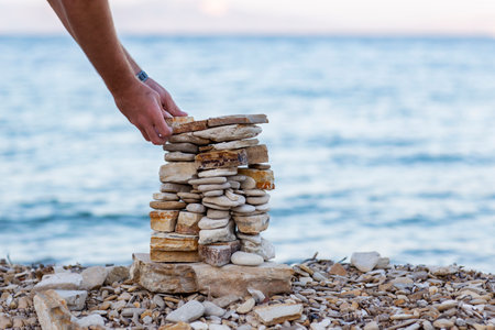 Person's hands stacking stones cains balanced structure on a pebble shoreline