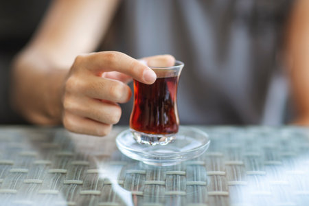 Close-up of man's hand holding glass of Turkish tea on reflection background table
