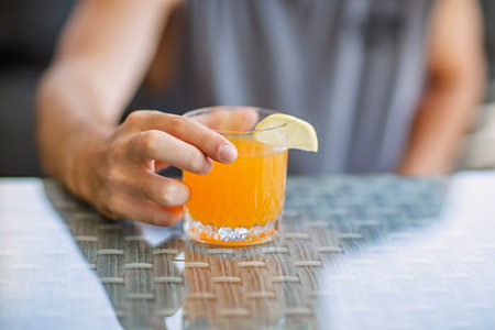Man hand holding glass of orange juice with slice of lemon on tableの写真素材
