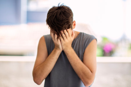 Portrait of a young man covering his face with his hands as if he's upset or frustrated, depression...