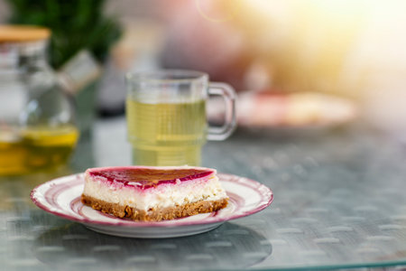 A piece of cheesecake on a plate and a cup of teaの写真素材