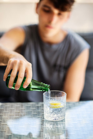 Young man pouring sparkling water into a glass with lemon.