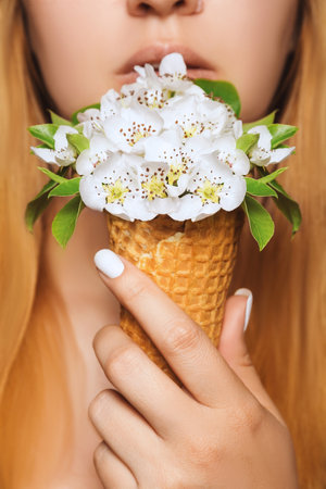 Ice cream made of flowers in a waffle cone is held by a young woman at lip level to eatの写真素材