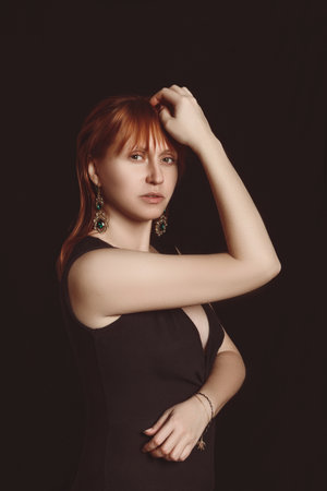 A young woman in a black blouse on a black background looks straight aheadの写真素材