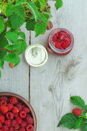 Raspberry berry fresh in a clay plate and in a jar for preservation on a wooden background, top viewの写真素材