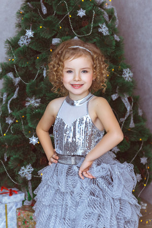 A beautiful curly-haired girl in an elegant dress is standing near the Christmas treeの写真素材