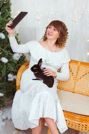 A woman in a white dress takes a selfie with a pad with a black rabbit. The relationship of a person with a petの写真素材