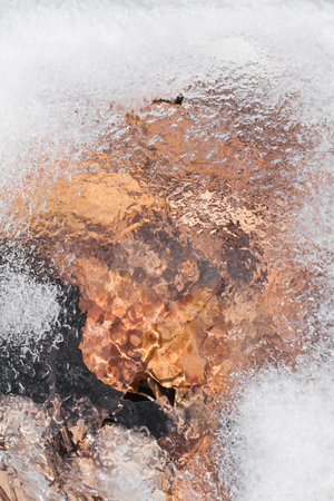 The texture of transparent ice with snow. Under the ice are leaves that create an interesting orange patternの写真素材