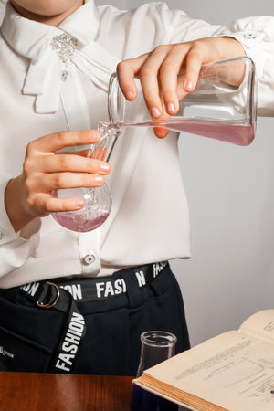 A schoolgirl conducts a chemical experiment based on a textbook. Pours pink liquid from one flask into another close-upの写真素材