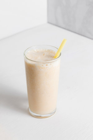 Milkshake with banana in a high transparent glass on a white background. A healthy drink for a dietの写真素材
