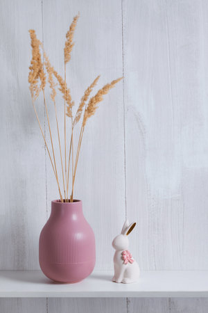 The shelf decor consists of a pink vase with dried flowers and a white porcelain rabbit with a pink bow with copy spaceの写真素材