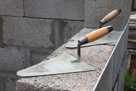 The concrete worker's trowels lie on a cinder block construction stone. It is used for bricklaying, as well as for measuring and applying cement mortarの写真素材