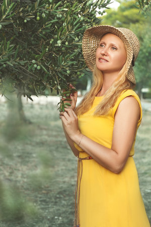 A girl in a hat stands near an olive treeの写真素材