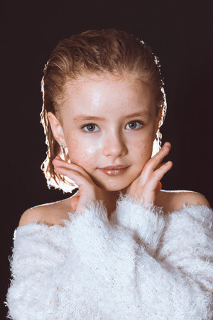 A model girl in a white blouse with sequins on the skin holds her hands near her face on a black backgroundの写真素材