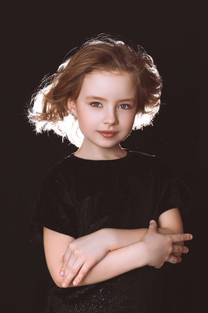A model girl in black clothes with flowing hair on a black background looks at the cameraの写真素材
