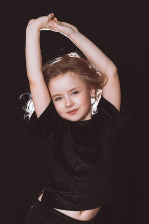 A model girl in black clothes on a black background pulls her hands upの写真素材