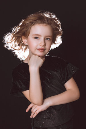 A model girl in black clothes with flying hair holds her hand under her chin on a black backgroundの写真素材