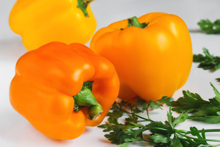 Three ripe orange sweet peppers and fresh green juicy parsley on a white tableの写真素材