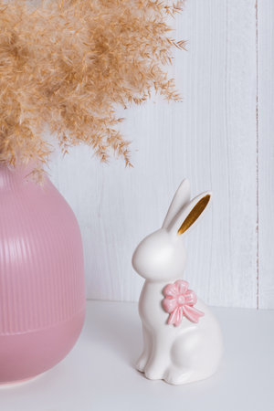 A white porcelain rabbit with a pink bow on a shelf next to a pink vase and a reedの写真素材